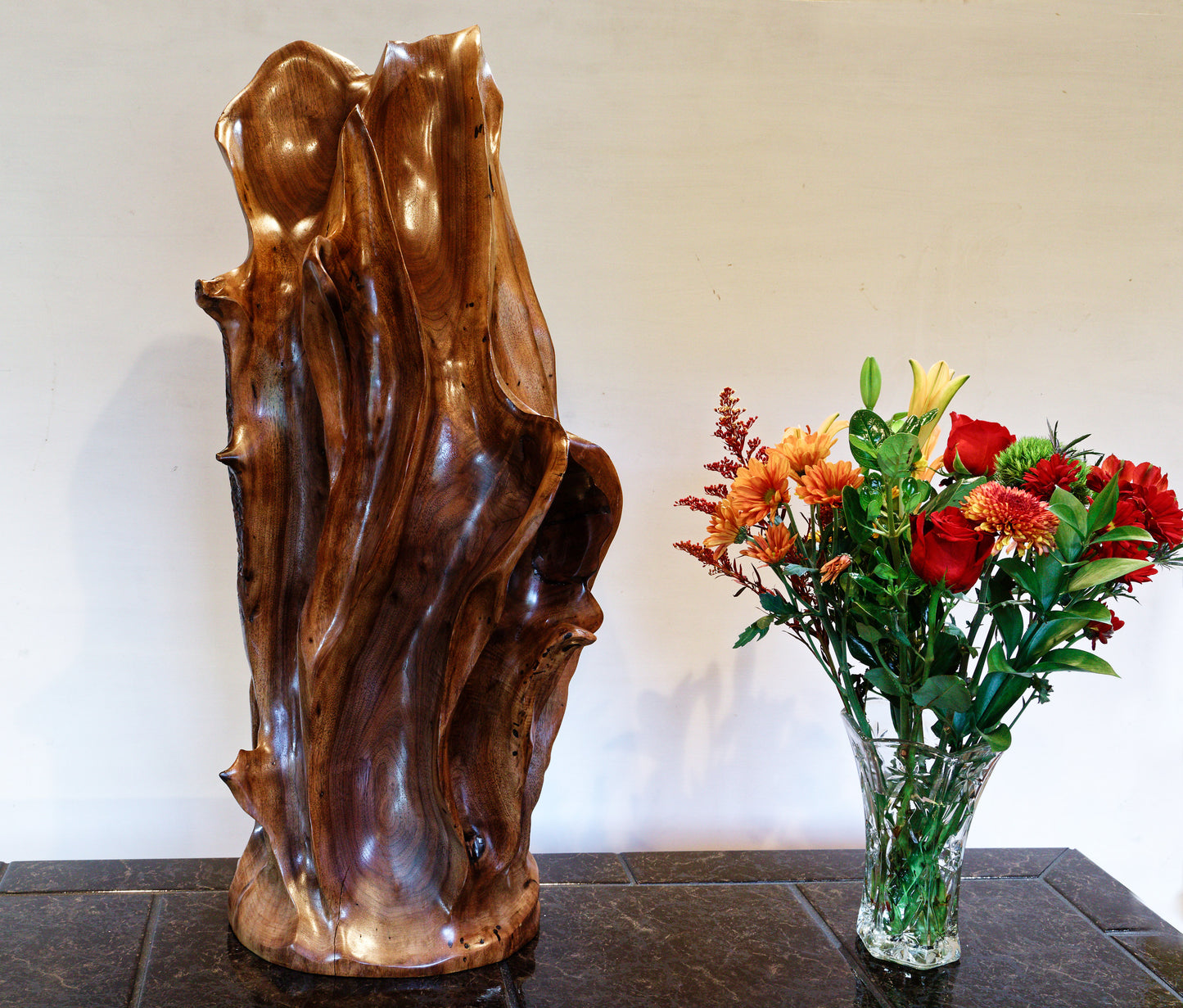 Beautiful brown tabletop and floor wooden sculpture 31.5" tall created from black Walnut wood, sitting beside a bouquet of red, yellow, green, flowers. It has freeform flowing lines showing amazing wood grain. The wood was rescued from a 24 inch diameter tree that died and fell in an Oregon winter storm.