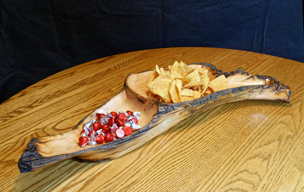 Front left view of a 2-part wooden Ponderosa pine bowl, platter, charcuterie board.  Rustic yet smooth, with live edge.  It is holding candy and chips and is 26.5" long x 11.5 x 4'' tall, and weighs 4.1 lbs., wild elegance.