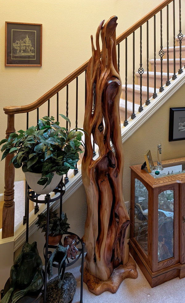 Tall and narrow free flowing Western red cedar sculpture with tan and reddish tones and richly colored grain patterns, 78 tall x 17 x 14'', 39 lbs.  On display in a home beside a staircase. 