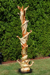 Potential rear view of a the completed 75.5" tall abstract branching indoor western juniper wood sculpture emphasizing the tree's original shapes.  It has beautiful rich grain patterns, natural unaltered golden tan and maroon colors, flowing flared lines with multiple grooves, intriguing hooked shapes.  One-of-a-kind 75.5" tall by 21" x 20'' floor sculpture.  It is smooth but has a few carefully conserved naturally rough surfaces. Seen here against a green conifer tree background.