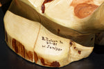 Closeup of a small section of the base of the wood sculpture showing the artist's name and item's information and wood species (western juniper). 