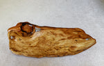 Top view of a 34 inch long natural burl wood serving board or tray with a polished finish, featuring a wavy grain pattern, displayed on a neutral gray textured background.