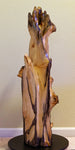 Possible left side view of a 36.7" tall twisted floor sculpture in front of a beige wall. Some live edge enhancements. One-of-a-kind exotic,  It was created from Pacific Ocean driftwood.  It has beautiful and exotic grain patterns with rich natural golden orange, tan, brown, black and gray colors (no stains or artificial colors).  The art piece measures 36.7 x 14.5 x 12.25'', 21.87 lbs.   RC Paulson Wildwood Art