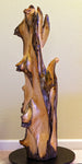 Possible right side view of a 36.7" tall twisted floor sculpture in front of a beige wall. Some live edge enhancements. One-of-a-kind exotic,  It was created from Pacific Ocean driftwood.  It has beautiful and exotic grain patterns with rich natural golden orange, tan, brown, black and gray colors (no stains or artificial colors).  The art piece measures 36.7 x 14.5 x 12.25'', 21.87 lbs.   RC Paulson Wildwood Art