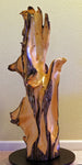 Possible front view of a 36.7" tall twisted floor sculpture in front of a beige wall. Some live edge enhancements. One-of-a-kind exotic,  It was created from Pacific Ocean driftwood.  It has beautiful and exotic grain patterns with rich natural golden orange, tan, brown, black and gray colors (no stains or artificial colors).  The art piece measures 36.7 x 14.5 x 12.25'', 21.87 lbs.   RC Paulson Wildwood Art
