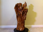 Side 1 view of an exotic brown and golden orange, black walnut wooden floor sculpture sitting on a home's beige carpet with a light colored wall in the background.  One-of-a-kind brown freeform abstract sculpture with an interwoven design with some parts resembling wild flowers or leaves.  It has beautiful grain colors and patterns.  It measures 32.5 x 17.5 x 17'', 36.8 lbs. 