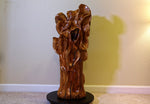 Right side of a glossy, sculptured wooden decor piece shaped like a gnarled tree trunk, displayed on a round black rotating base (not included) in front of a beige wall. 