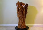 Side 4 or left side of a glossy, sculptured wooden decor piece shaped like a gnarled tree trunk, displayed on a round black rotating base (not included) in front of a beige wall. 