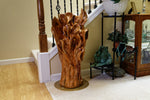 Exotic wood sculpture on the floor beside the start of a home's staircase and a frog statue and display case.  One-of-a-kind brown and golden orange, black walnut floor sculpture with a freeform abstract interwoven design with some parts somewhat resembling wild flowers or leaves.  It has beautiful grain patterns.  It measures 32.5 x 17.5 x 17'', 36.8 lbs.  Satin finish. 