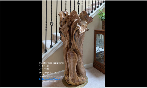 Freeform one-of-a-kind exotic maple brownish gold, wood floor sculpture standing beside a home's staircase.  The sculpture is asymmetrical with twists and turns, grooves, see through sections, and unique cup-like shapes at the top which are a bit like wildflowers.  41.5 tall x 24 wide x 16''