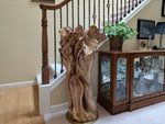 Freeform one-of-a-kind exotic maple brownish gold, wood floor sculpture standing beside a home's staircase and fancy glassware display cabinet.  The sculpture is asymmetrical with twists and turns, grooves, see through sections, and unique cup-like shapes at the top which are a bit like wildflowers.  41.5 tall x 24 wide x 16''