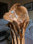 Close up view of the top of a wildflower-like large wooden sculpture in a living room setting.  Sculpture has exotic colorful grain patterns. 