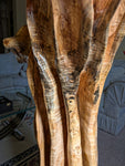 Close up view of the fluted sides of a wildflower-like large wooden sculpture in a living room setting.  The sculpture has exotic colorful grain patterns showing brown, gold, tan, and black stripes. 
