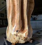 Close up view of the base of a large wooden sculpture in a living room setting.  Sculpture has exotic colorful grain patterns. 