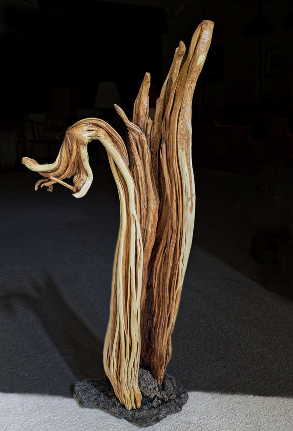 Wooden irregular sagebrush sculpture mounted on a lava rock base, on a dark background